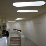 Adalberto Dias's design of the Autonomous Section of Mechanical Engineering at the University of Aveiro showcasing an interior with a composite material ceiling, modern light fixtures, and cylindrical elements.