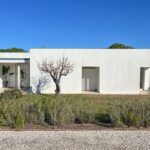 Álvaro Siza Vieira's 14 Villas at Bom Sucesso Resort showcasing a modern design with concrete walls, large doors, and surrounding grass and shrubs.