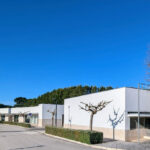 Álvaro Siza Vieira's Commercial Area at Bom Sucesso Resort showcasing a modern design with concrete structures, composite materials, a landscaped walkway, and a shaded driveway leading to the corporate headquarters.