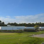 Álvaro Siza Vieira's Nave Lagoa - Event Space at Bom Sucesso Resort showcasing a modern design with a sleek, minimalist structure surrounded by lush grass and plants in a rural landscape.