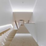 Álvaro Siza Vieira's Nave Lagoa at Bom Sucesso Resort showcasing a modern event space with a triangular design, featuring wooden flooring, composite material stairs, and a plaster ceiling.