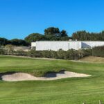 Álvaro Siza Vieira's Nave Lagoa - Event Space at Bom Sucesso Resort showcasing a modern design with a sleek, minimalist structure surrounded by landscaped grass and open meadow areas.