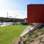 Eduardo Souto de Moura's 6 Red Lakeside Villas at Bom Sucesso Resort showcasing a modern design with a reflective pond, landscaped lawn, and wetland features in the backyard.