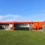 Luís Pessanha Moreira's 27 Row Houses at Bom Sucesso Resort showcasing a modern design with an orange exterior, lush lawn, spacious backyard, eco-friendly features, and a swimming pool surrounded by artificial turf.