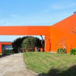 Luís Pessanha Moreira's 27 Row Houses at Bom Sucesso Resort showcasing a vibrant red and orange exterior with lush garden landscaping and a well-maintained lawn.