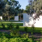 Manuel Aires Mateus's 7 Row Houses at Bom Sucesso Resort showcasing a modern design with a minimalist aesthetic, surrounded by lush vegetation, trees, and a well-maintained lawn.