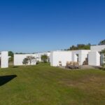 Manuel Aires Mateus's 7 Row Houses at Bom Sucesso Resort showcasing minimalist design with a flat roof, expansive glass façades, and integrated landscaping blending with the surrounding grass and meadow.