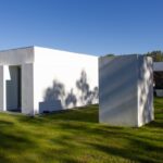 Manuel Aires Mateus's 7 Row Houses at Bom Sucesso Resort showcasing a modern architectural design with concrete structures, expansive glass façades, and a surrounding grassy landscape.