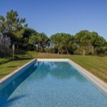 Manuel Aires Mateus's 7 Row Houses at Bom Sucesso Resort showcasing a modern design with a blue swimming pool, composite material structures, landscaped gardens, and water features reflecting the surrounding resort environment.