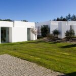 Manuel Aires Mateus's 7 Row Houses at Bom Sucesso Resort showcasing a modern design with a landscaped garden, lush grass, and neatly trimmed hedges.
