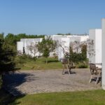 Manuel Aires Mateus's 7 Row Houses at Bom Sucesso Resort showcasing a minimalist design with a landscaped garden, grass-covered yard, and neatly arranged shrubs.