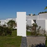 Manuel Aires Mateus's 7 Row Houses at Bom Sucesso Resort showcasing a modern urban design with concrete structures, daylighting, and landscaped yards bordered by hedges.