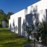 Manuel Aires Mateus's 7 Row Houses at Bom Sucesso Resort showcasing a modern design with concrete structures, composite materials, and integrated landscaping providing shade and daylighting in the backyard.