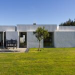 Manuel Aires Mateus's 7 Row Houses at Bom Sucesso Resort showcasing a modern design with composite materials, expansive glass façades, and landscaped lawns surrounded by grassy meadows.