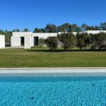 Manuel Aires Mateus's 7 Row Houses at Bom Sucesso Resort showcasing a modern villa design with a swimming pool, landscaped garden, and artificial turf surrounded by evergreen plants.