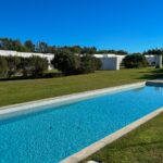 Manuel Aires Mateus's 7 Row Houses at Bom Sucesso Resort showcasing a modern design with composite materials, a blue swimming pool, landscaped gardens, and a water feature surrounded by a well-maintained lawn.