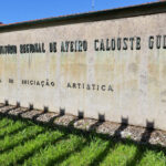 Noémia de Azevedo Coutinho's Conservatório de Música de Aveiro Calouste Gulbenkian showcasing a modern concrete structure with a commemorative plaque and surrounding palm trees.