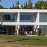 Nuno Graça Moura's 24 Row Houses at Bom Sucesso Resort showcasing a modern estate design with landscaped surroundings, shaded outdoor structures, and conifer trees.