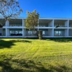 Nuno Graça Moura's 24 Row Houses at Bom Sucesso Resort showcasing a modern villa design with a landscaped garden, expansive lawn, and shaded areas.