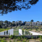 Nuno Graça Moura's 24 Row Houses at Bom Sucesso Resort showcasing a modern design with a landscaped garden, shrubbery, and a walkway integrated into the plantation surroundings.