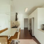 Nuno Graça Moura's 8 Villas at Bom Sucesso Resort showcasing a modern interior design with wooden flooring, sleek furniture, and a minimalist kitchen featuring a light fixture and countertop.