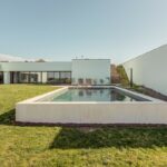 Nuno Graça Moura's 8 Villas at Bom Sucesso Resort showcasing modern architecture with concrete structures, landscaped gardens, and composite materials, surrounded by well-maintained lawns and artificial turf.