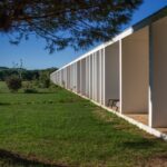 Nuno Graça Moura's Bar Code 2 - 12 Row Houses at Bom Sucesso Resort showcasing a modern design with a linear arrangement, surrounded by lush grass and plantation, casting distinct shadows on the lawn.