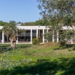 Nuno Graça Moura's Bar Code 2 - 12 Row Houses at Bom Sucesso Resort showcasing a modern design with a columned structure, landscaped garden, and expansive lawn surrounded by trees.