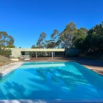 Nuno Graça Moura's Pool Bar at Bom Sucesso Resort showcasing a modern design with a blue swimming pool, composite materials, shaded areas, and integrated landscaping in an eco-friendly resort setting.
