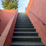 Nuno Graça Moura's Tennis Club at Bom Sucesso Resort showcasing a modern design with concrete stairs, composite materials, and a red handrail, enhanced by daylighting and shadows.