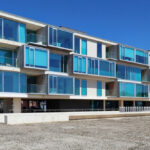 RVdM Arquitectos' ORIZZONT Residential Building showcasing a modern design with blue-tinted glass façades, shaded balconies, and strategic daylighting elements.