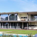 Rui Passos's design of The Ken Houses - 7 Villas at Bom Sucesso Resort showcasing a modern facade with a prominent porch, large doors, and balconies, highlighting the estate's contemporary architectural design.