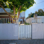 Alcino Soutinho’s Unifamiliar em Paços de Brandão showcasing a modern home with concrete walls, metal gate, iron fencing, and composite material elements casting distinct shadows.
