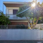 Alcino Soutinho’s Unifamiliar em Paços de Brandão showcasing a modern home with composite material walls, a balcony with shading elements, a gated fence, and ample daylighting.