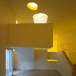 Álvaro Siza Vieira and Eduardo Souto de Moura’s Museum of International Contemporary Sculpture interior showcasing plaster walls and ceiling with minimalist light fixtures casting dynamic shadows.