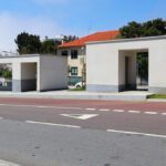 Álvaro Siza Vieira’s Abrigos da Linha de Metro-Bus “Boavista-Império” showcasing minimalist concrete shelters with composite material roofing, integrated into an asphalt road surface and public sidewalk area providing shaded public utility space.