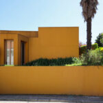 Álvaro Siza Vieira’s Casa António Carlos Siza showcasing vibrant yellow and orange painted walls with surrounding palm trees.