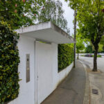 Álvaro Siza Vieira’s Casa Ferreira da Costa showcasing a minimalist concrete façade with integrated shading elements, surrounded by shrubs and hedges along a daylighted sidewalk and walkway.