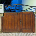 Álvaro Siza Vieira’s Casa Luís Rocha Ribeiro showcasing a wooden gate and door with rich wood stain, metal and iron hardware, hardwood planks, and a driveway bordered by a wooden fence.