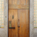 Álvaro Siza Vieira’s Casa dos Pais showcasing a brown stained hardwood door with a yellow composite material wall and a visible door handle.