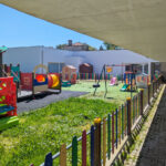 Álvaro Siza Vieira’s Centro Social e Paroquial de Sao Miguel de Ceide showcasing a community centre with a shaded courtyard, artificial turf, outdoor play equipment, and a public space designed for kindergarten activities.