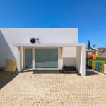 Álvaro Siza Vieira’s Centro Social e Paroquial de Sao Miguel de Ceide showcasing a minimalist concrete and plaster façade with composite material walls, shaded doorways, and a driveway integrated into a residential area.