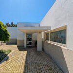 Álvaro Siza Vieira’s Centro Social e Paroquial de Sao Miguel de Ceide showcasing a concrete and composite material structure with tiled flooring, shaded areas, and strategic daylighting enhancing the minimalist design.