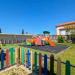 Álvaro Siza Vieira’s Centro Social e Paroquial de Sao Miguel de Ceide showcasing a landscaped courtyard with artificial turf, outdoor play equipment, shaded areas, and a modern structure integrating leisure and community spaces.