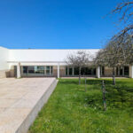 Álvaro Siza Vieira’s Centro de Estudos Camilianos showcasing a concrete structure with composite material elements, shaded courtyard, landscaped lawn, tiled walkway, and ample daylighting.