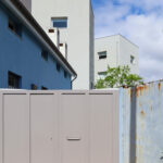 Álvaro Siza Vieira’s Edificio de Escritónos showcasing a minimalist concrete structure with composite material elements and a prominent gate entrance.