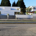 Álvaro Siza Vieira’s Moradias na Avenida da Boavista showcasing modern residential architecture with concrete façades, balconies, composite materials, and urban design elements including home fencing and shaded suburban surroundings.