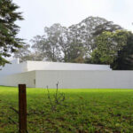 Álvaro Siza Vieira’s Piscina da Quinta da Conceição showcasing a minimalist concrete structure with a composite material pool, surrounded by landscaped lawn and shaded areas, emphasizing daylighting and shadow play.