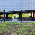Casa Sacerdotal de São Martinho de Dume by André and António Fontes showcasing a modern mesh fence and shaded walkway designed for optimal daylighting.