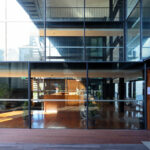 Casa Sacerdotal de São Martinho de Dume by André and António Fontes showcasing a modern interior with hardwood flooring, metal ceiling elements, glass partitions, and composite material finishes.